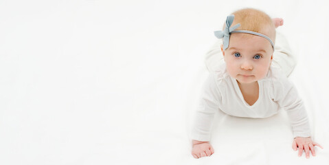 Cute caucasian baby girl with blue bow on head, looking at camera, white clothes on white background. Copy space for text, banner.