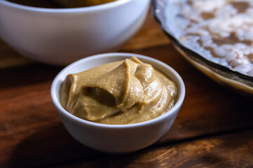 Fresh homemade organic mustard in bowl on wooden background top view