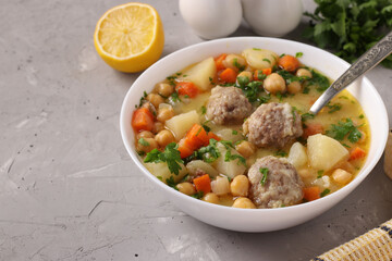 Turkish soup with chickpeas, meatballs and vegetables in a white bowl on a gray background. Close-up. Copy space