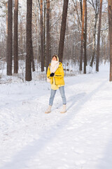 Beautiful young cheerful woman in a snowy landscape winter forest having fun rejoices in winter and snow in warm clothes, scarf and jeans