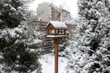 Snow-covered bird feeder in the courtyard of a village house on  cloudy winter day.
