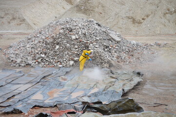 Bauarbeiter in gelbem Anzug auf Baustelle sprüht Wasser 1