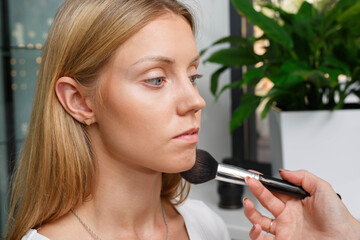 The process of creating makeup. Makeup artist working with a brush on the face of the model.