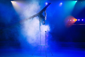 A man of athletic build performs complex gymnastic exercises in the circus arena.
