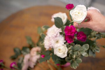 Hand holding beautiful blooming white rose over a bunch of colorful flowers and fresh green leaves at the wooden table, depth od filed. Florist arrangement flora at home for anniversary gift. Top view