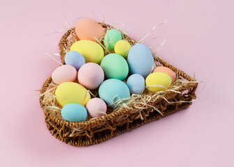 Fototapeta na wymiar Pastel multi-colored Easter eggs in a basket in the shape of a heart on a pink background. Place for text. Greeting card.