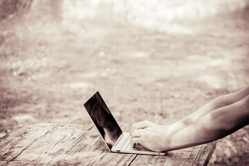 Young man working with laptop in nature. Man's hands on notebook computer. Business person at workplace. Freelance. Outdoor, summer, close up. Sepia. Copy space.