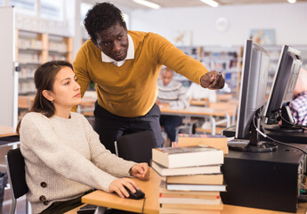 Portrait of confident man librarian assisting woman in library