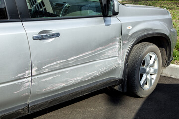 car with a scratched door and a dent in the fender, a gray car with damage after an accident close-up.