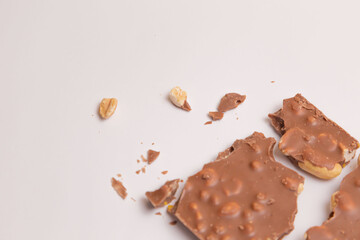 Milk chocolate with nuts lies broken near a knife on a white background. Top view. Place for an inscription. Advertising. Close plan. Food. Sweets