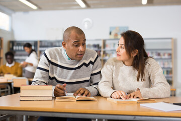 Positive young adults communicating while preparing to exam in library