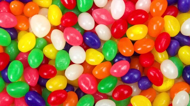 HD video above zooming in on background of many brightly colored jelly beans in a rainbow of colors. Popular candy for Easter.
