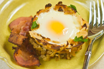 top, close distance of a s sunny side up egg on homemade basked of potato strings with bacon on a round, yellow dish 