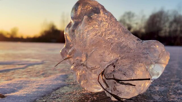 Transparent shining clear ice close-up sparkling on frozen windy wild lake surface in sunset light. Cold winter nature background