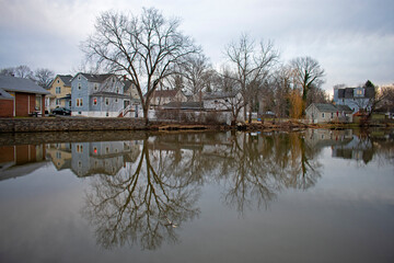 Fototapeta na wymiar Reflections of barren trees and houses in the still waters of Peddie lake in Hightstown, New Jersey, on a cloudy afternoon -01