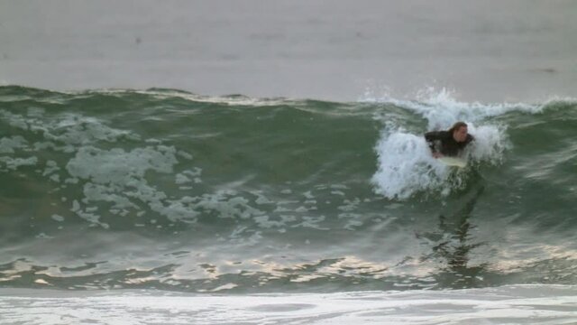 This slow motion video shows a surfer catching an ocean wave on his board and the wiping out.