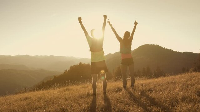 Adventurous couple running uphil reaching the top of a hill and put their hands high in the air - success, reaching goal, moutain view, trail run in slow motion. 