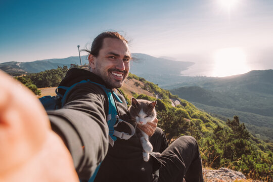 A man tourist with a cat makes a selfie in the mountains at dawn - Powered by Adobe