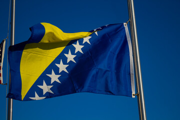 A Bosnian flag on a pole waves in the wind on a sunny day.