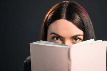 Beautiful brunette girl looking from behing the book in pink cover.