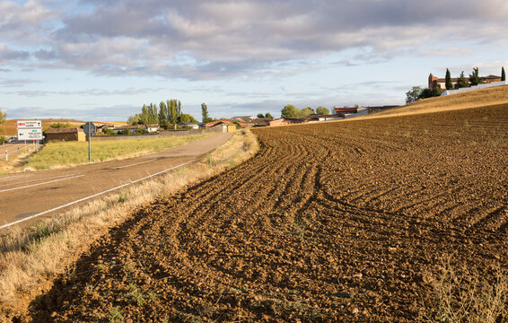 a paved road on a plowed field entering Ledigos village, province of Palencia, Castile and Leon, Spain
