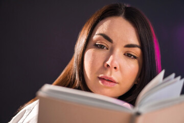 Young brunette girl is reading exciting book over black background.