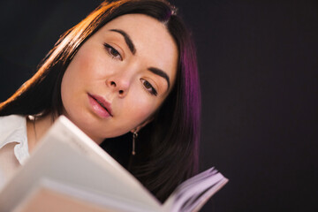 Young brunette girl is reading exciting book over black background.