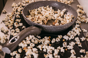 Obraz na płótnie Canvas Making popcorn in a frying pan without a lid, popcorn scattered on the table, a mess in the kitchen, popcorn day