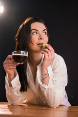 Portrait of young woman with cup of coffee and macaroon over black background.