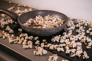 Obraz na płótnie Canvas Making popcorn in a frying pan without a lid, popcorn scattered on the table, a mess in the kitchen, popcorn day