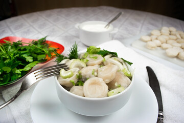 Bowl of cooked homemade dumplings garnished with green dill and parsley leaves with a fork and knife. Close-up.