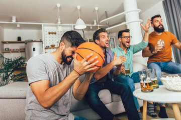 Happy friends or basketball fans watching basketball game on tv and celebrating victory at home.
