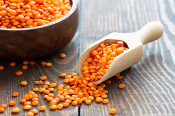 Uncooked raw red lentil in wooden shovel or bowl on wooden background, (Lens culinaris)