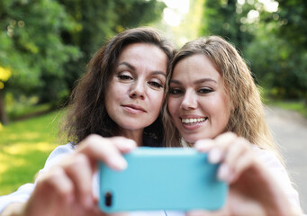 Lifestyle, family and people concept: mature mother and adult daughter are doing selfie by mobile phone in summer park