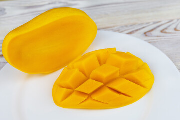 ripe and juicy mango gold cut in half on a plate on a white wooden background.