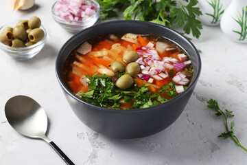 Greek tomato soup with vegetables, green olives and white beans in a dark bowl on a gray background. Closeup