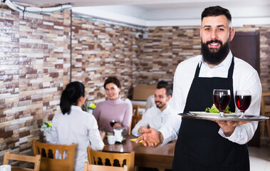 Fototapeta na wymiar friendly waiter serving dear restaurant guests at table