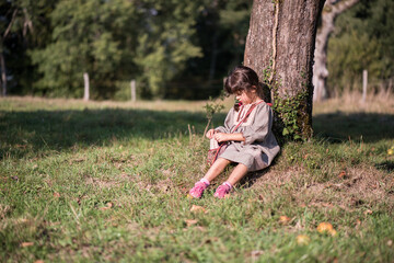 Country girl sitting under a tree in a rustic landscape.