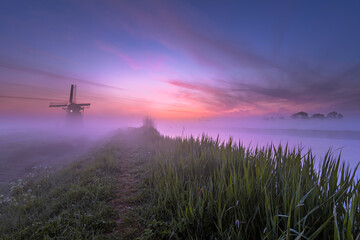 sunrise on a foggy morning in a Dutch landscape with a windmill
