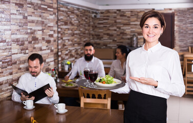 Pretty waitress greeting customers at table in restaurant
