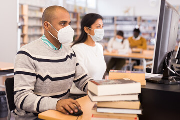 Portrait of hispanic man in protective mask studying in computer class in public library during...