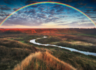 Amazing rainbow over the small rural river. autumn morning

