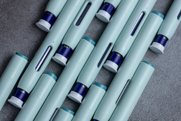 Slanted rows of syringe self application pens on rustic gray kitchen counter background. Studio medical equipment still life concept with auto-injector disposable devices.