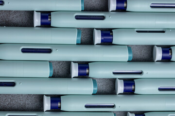 Front to back rows of syringe self application pens against a rustic textured gray background. Studio medical equipment still life concept with auto-injector disposable devices.