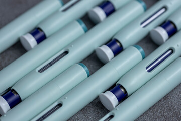 Closeup of slanted rows of syringe self application pens on rustic gray kitchen counter background. Studio medical equipment still life concept with auto-injector disposable devices.