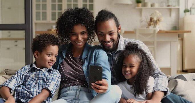 Carefree family little kids enjoy weekend seated on couch at home with smartphone, watching funny videos online, use cool mobile app on device laughing feels happy. Modern tech, fun, free time concept