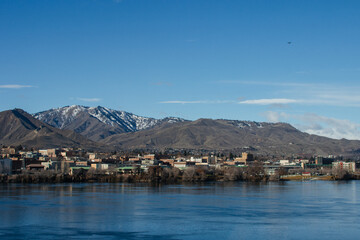 A city behind a wide river against a background of blue mountains on a sunny day against a background of a bright blue sky
