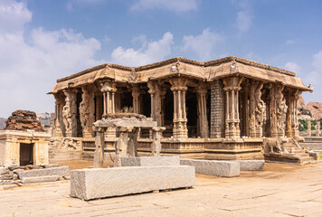 Hampi, Karnataka, India - November 5, 2013: Vijaya Vitthala Temple. Smaller side brown stone mandapam hall with elephant steps and sculpted pillars under blue cloudscape.