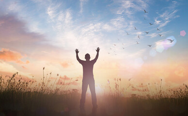Praise and worship God concept: Silhouette of healthy man raised hands at meadow sunset background