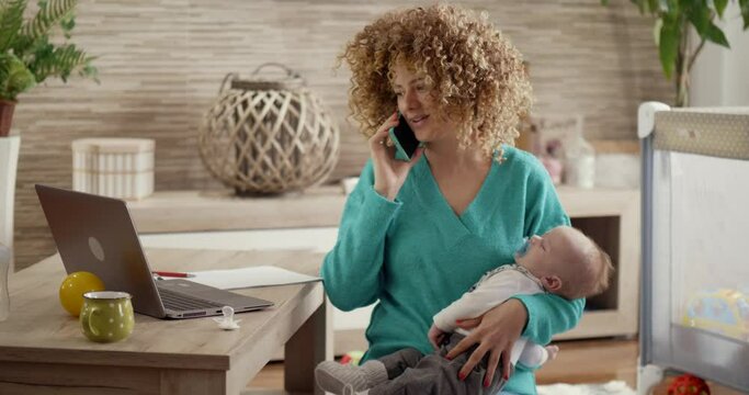 A young mother is talking on her cell phone, a lady is holding a baby. A woman is combining a decree and motherhood. Candid authentic and real life mom working and parenting